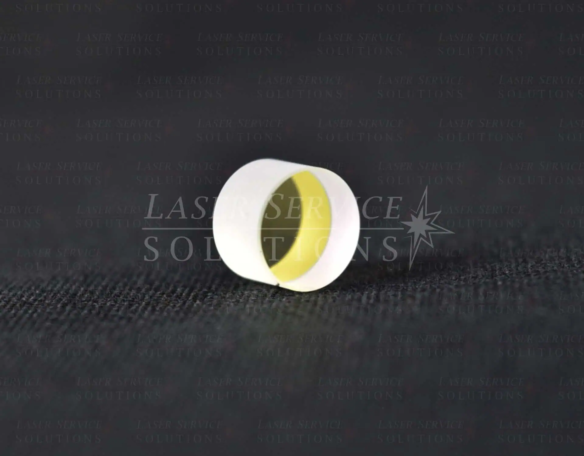 A Candela Vbeam Perfecta OC Mirror, small and cylindrical with a yellow reflective coating, rests on a textured black surface. The mirror is positioned horizontally, displaying its coated interior.
