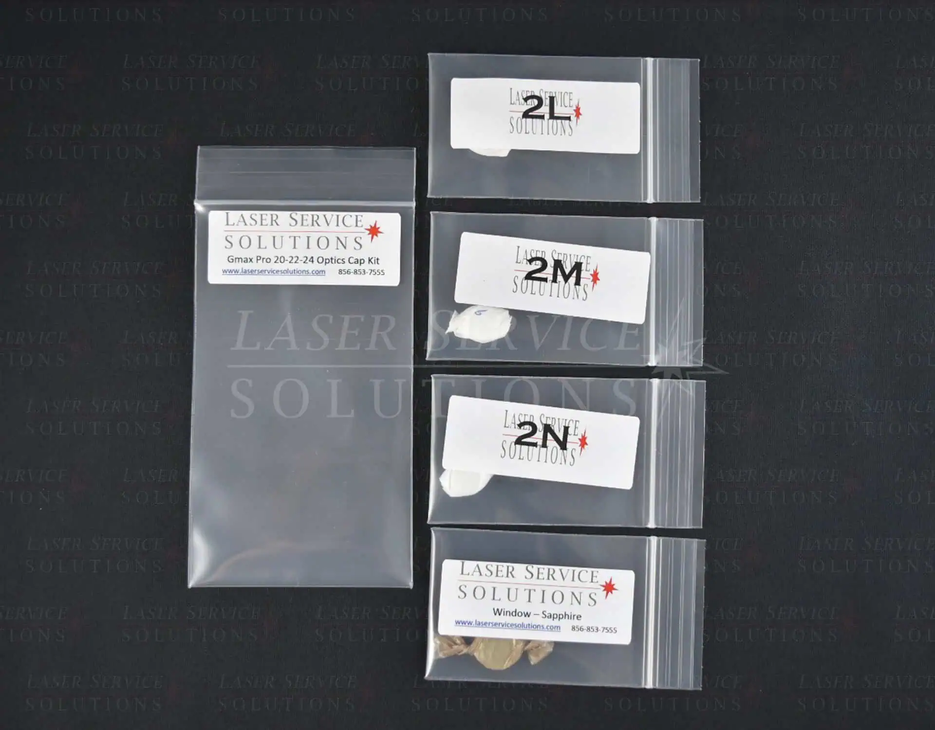 Five labeled plastic bags from Laser Service Solutions’ Candela Gmax Pro Optics Cap Lens Kit are arranged on a black background, featuring a larger empty bag and four smaller ones labeled with different codes and contents.