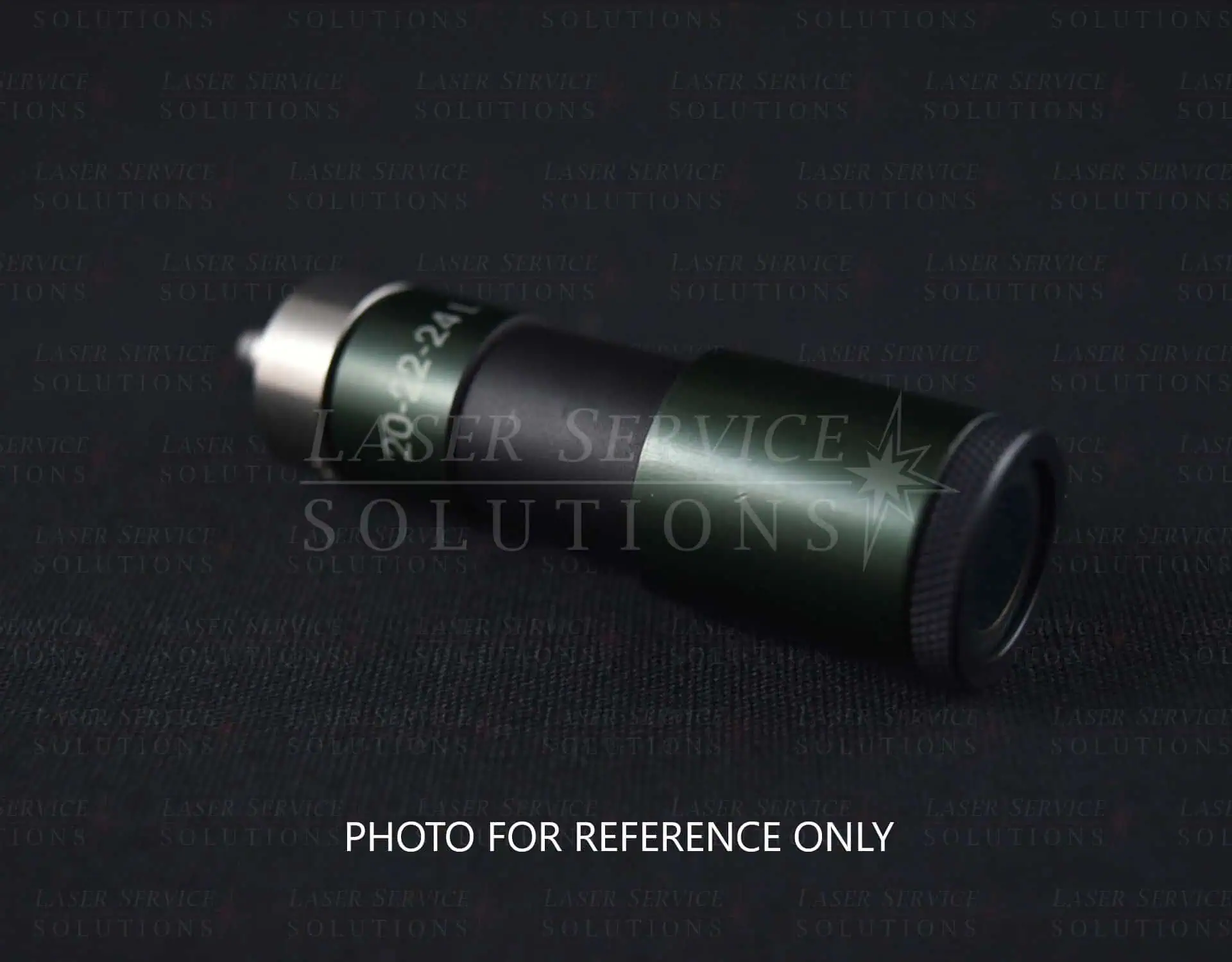 A Candela Gmax Pro Optics Cap Lens Kit, featuring a cylindrical black and green metal design, is shown lying on a dark surface with the text “PHOTO FOR REFERENCE ONLY” displayed below it.