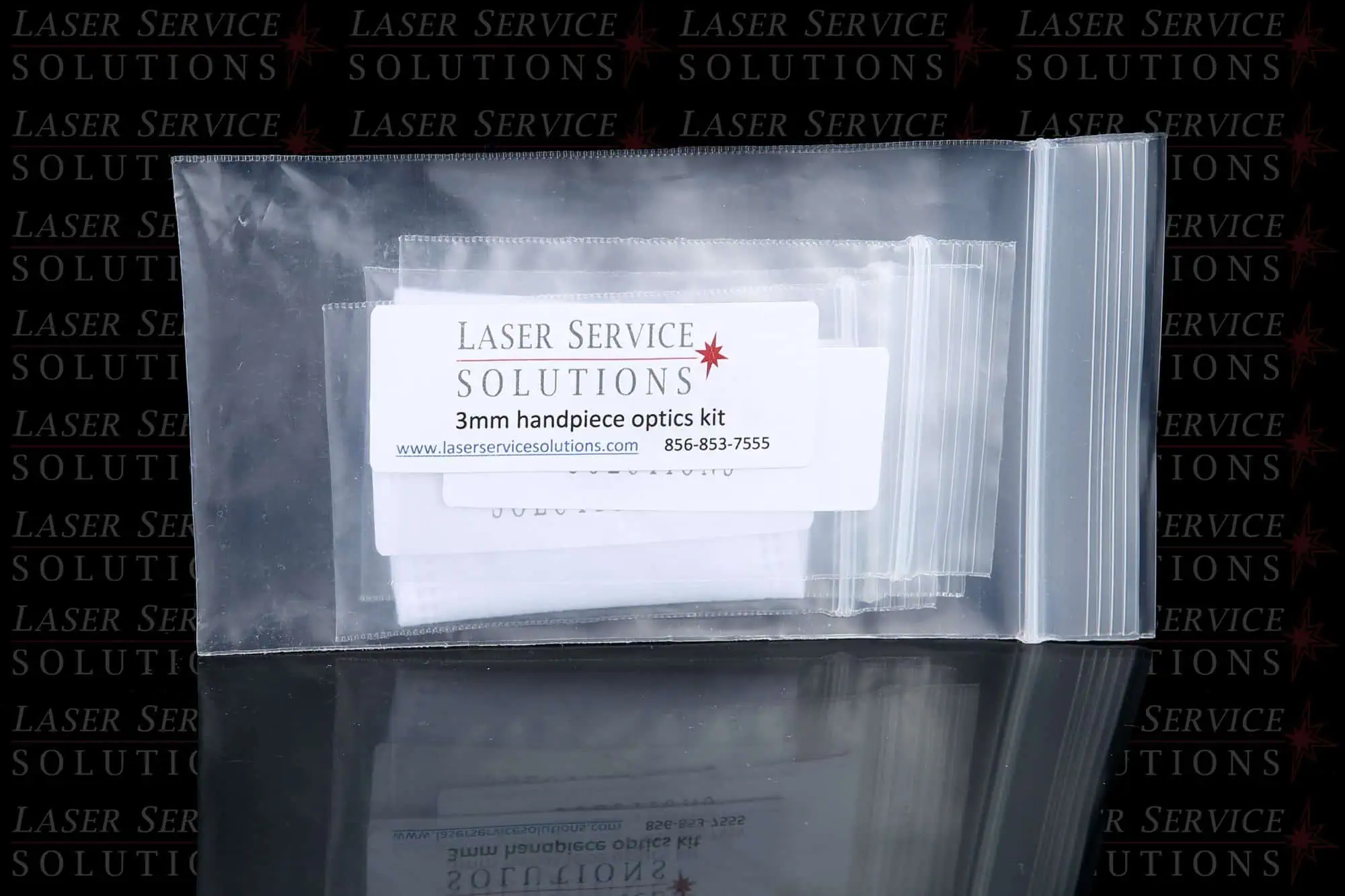 A clear ziplock bag labeled Laser Service Solutions Elite+ Handpiece Optics Kit, featuring a website and phone number, displayed on a reflective surface with the company logo in the background.