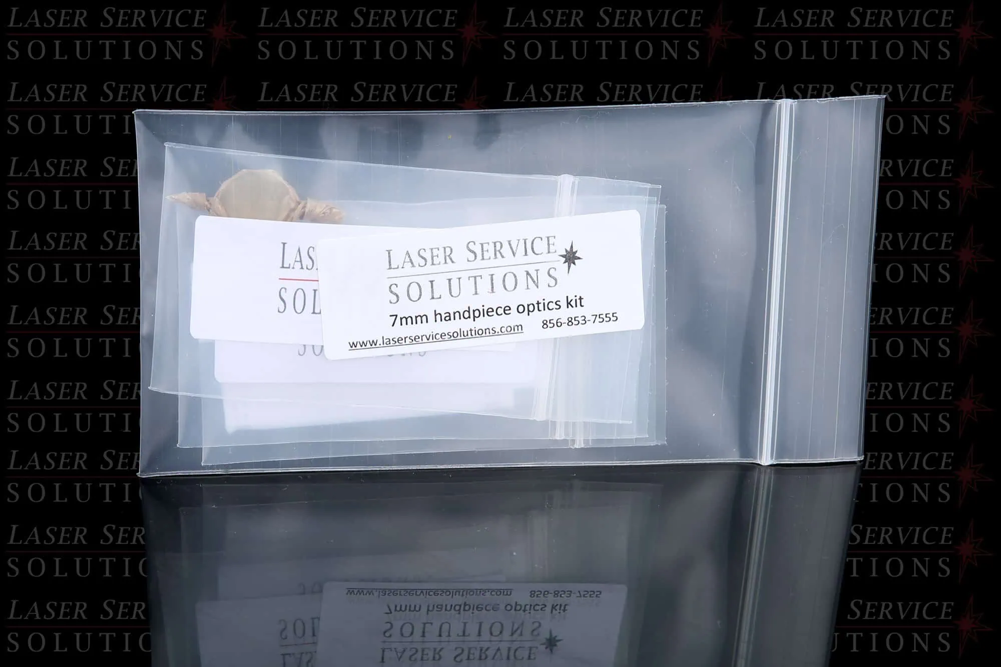 A clear plastic bag contains labeled cards for the Elite Handpiece Optics Kit, designed for a 7mm handpiece from Laser Service Solutions. The background features the company’s name repeatedly, and contact details are visible on the label.