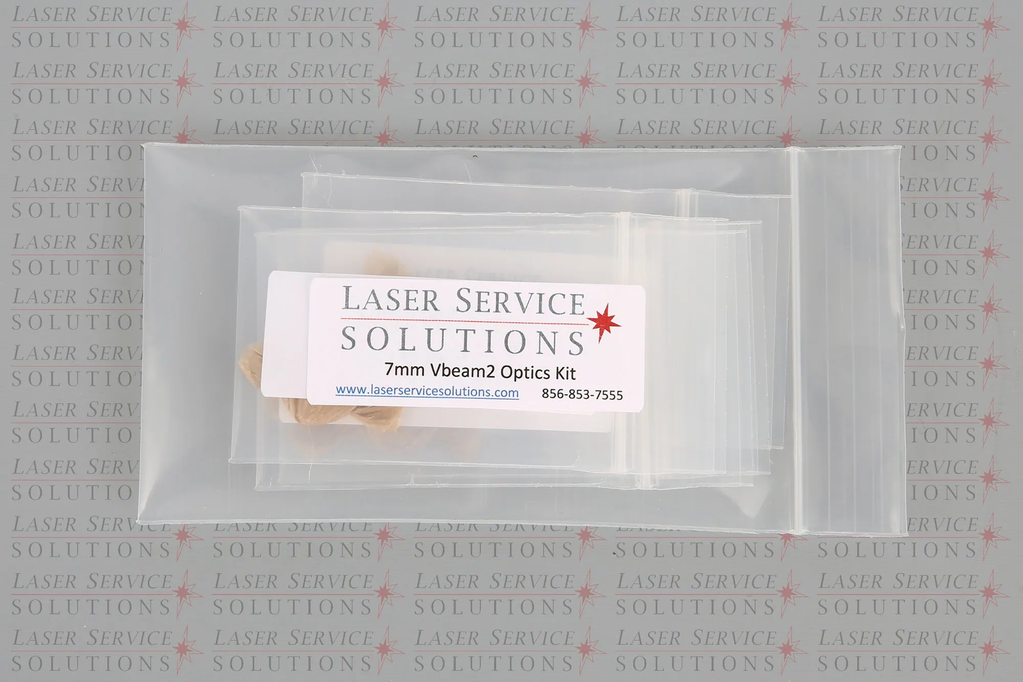 A plastic bag labeled Laser Service Solutions Candela Vbeam Perfecta Optics Kits with contact info, placed on a background printed repeatedly with Laser Service Solutions.