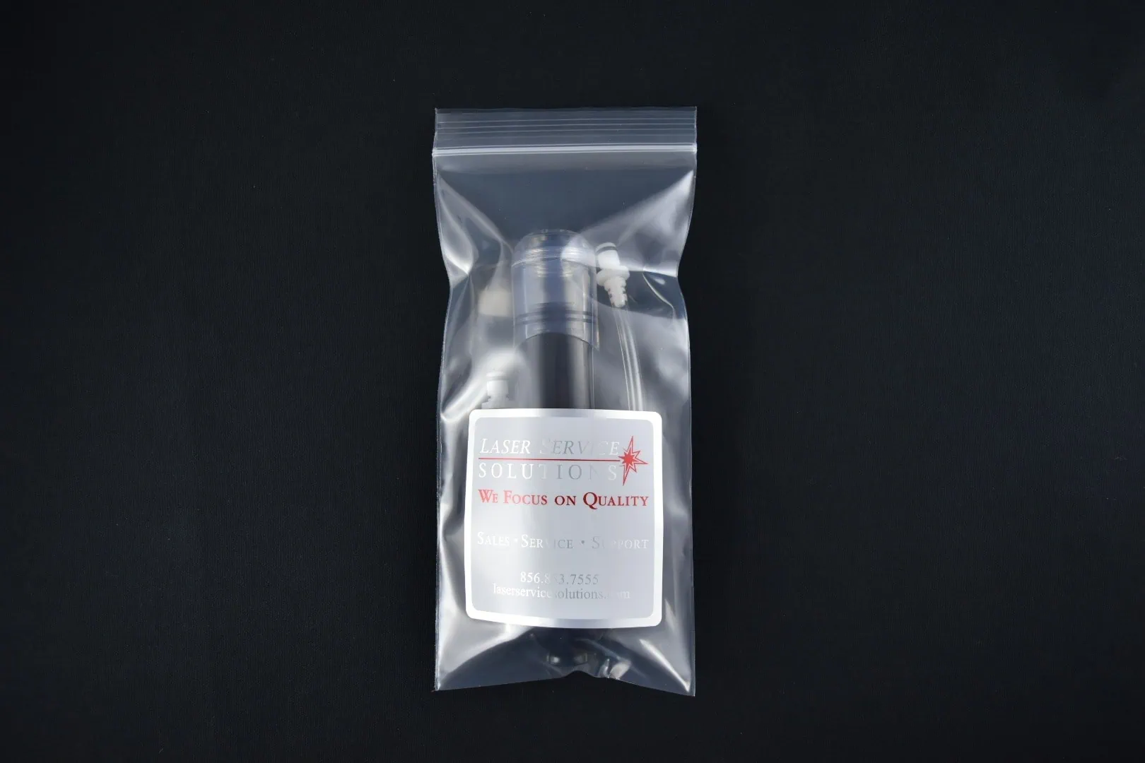 A Soprano Handpiece Drain Kit, featuring a small black bottle with a white label that reads “Laser Service Solution, We Focus on Quality,” is shown in a clear resealable bag along with a cotton swab and tube, all set against a plain black background.