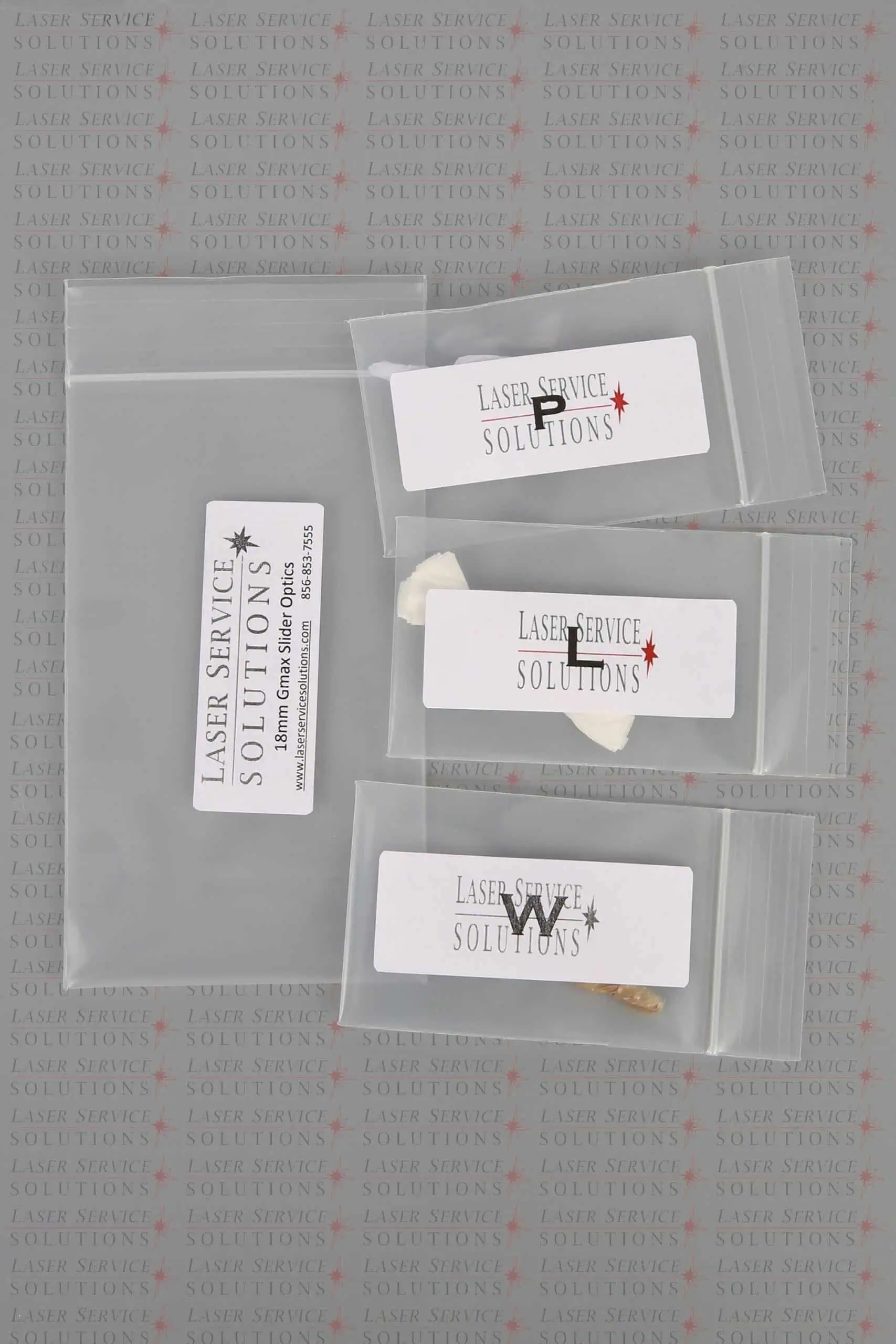 Three small labeled plastic bags containing stones and one larger labeled bag, all displayed on a background featuring the repeated Laser Service Solutions logo, as shown with the Candela Gmax Slider Optics Kits.