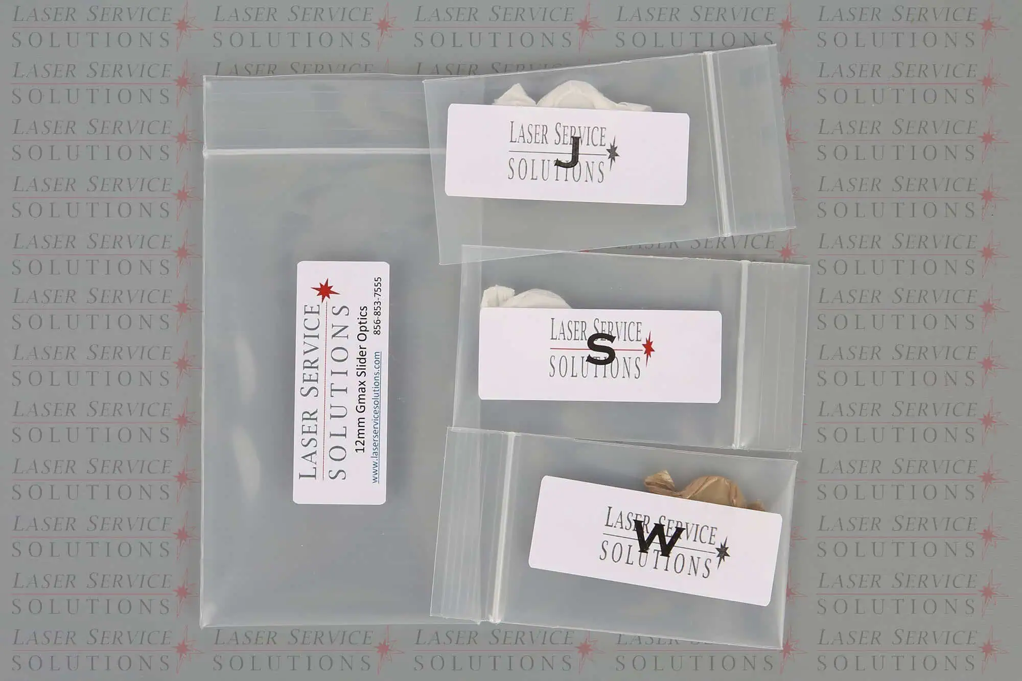 Four plastic bags—three small and one larger zip bag—all labeled Laser Service Solutions, are displayed on a background featuring the repeated Laser Service Solutions logo. Each bag contains components from the Candela Gmax Slider Optics Kits, visible as small metallic objects.