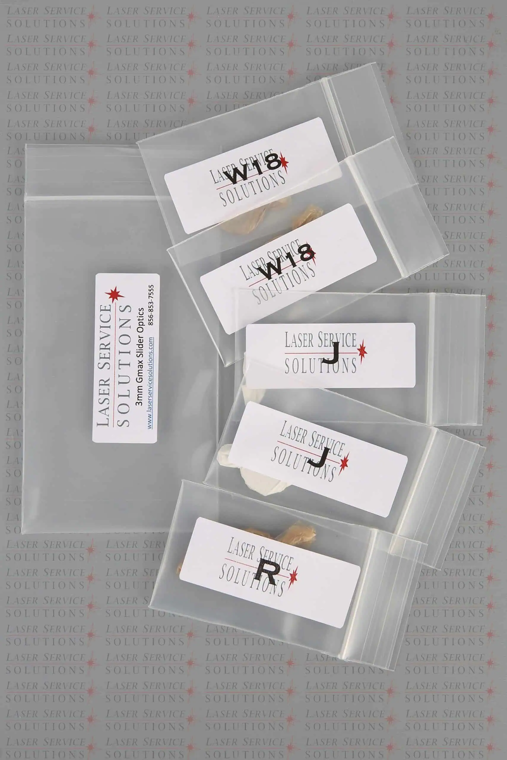 Six small clear bags labeled “Laser Service Solutions,” each containing a Candela Gmax Slider Optics Kit component, are arranged on top of a larger labeled bag. The background features a repeating Laser Service Solutions logo in faint gray and red text.