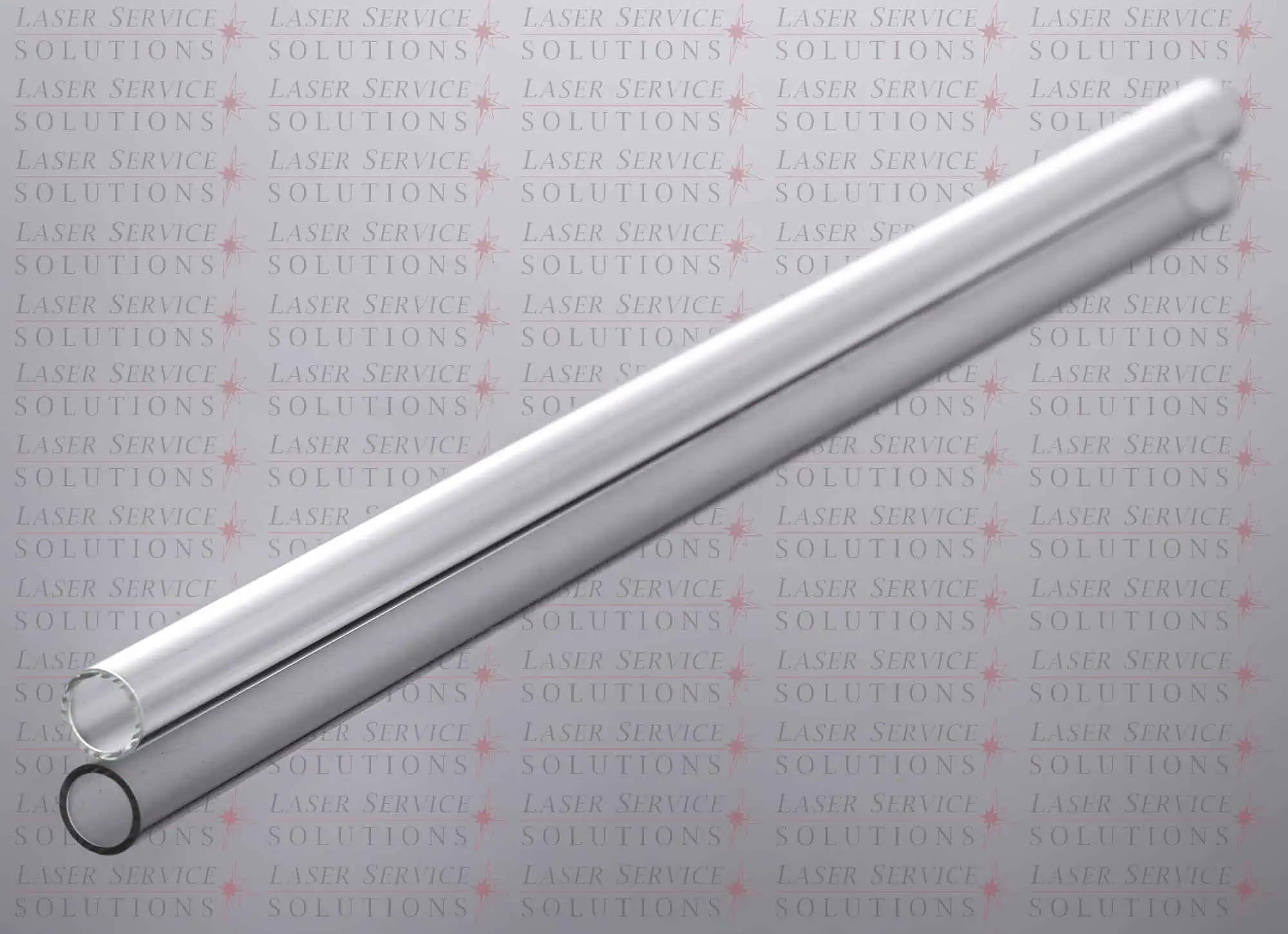 Two Candela Vbeam Perfecta Flow Tubes, made of clear cylindrical glass, are placed diagonally on a surface with faint Laser Service Solutions logos repeatedly printed in the background.