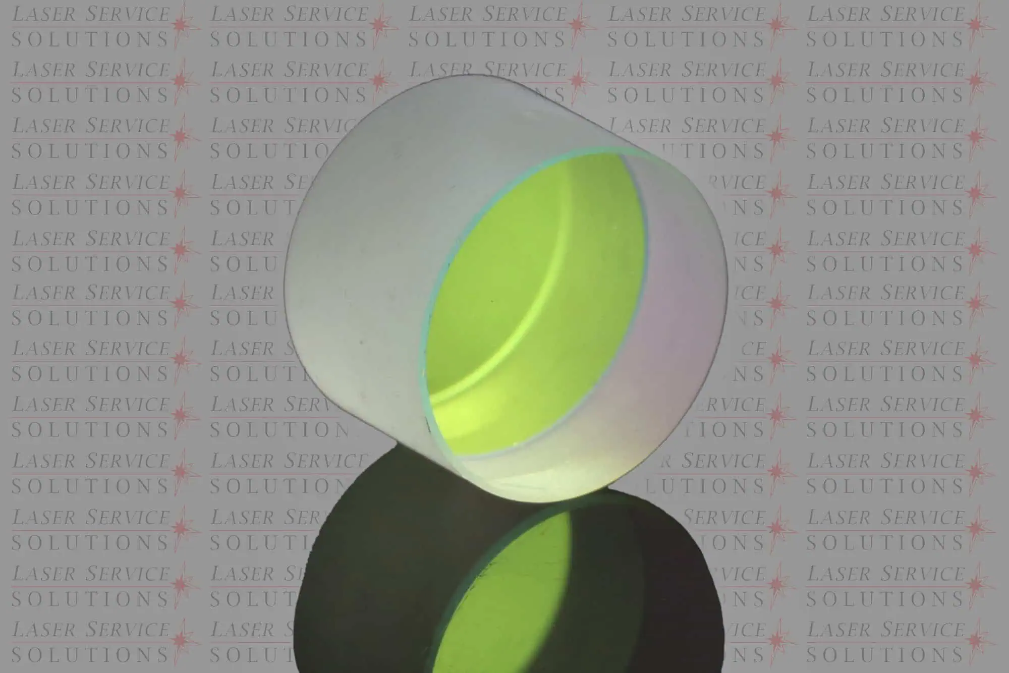 Transparent cylindrical Candela Vbeam Perfecta HR Mirror with a slight green tint, placed on a reflective black surface. The background features repeated text: LASER SERVICE SOLUTIONS in a pattern with red stars.