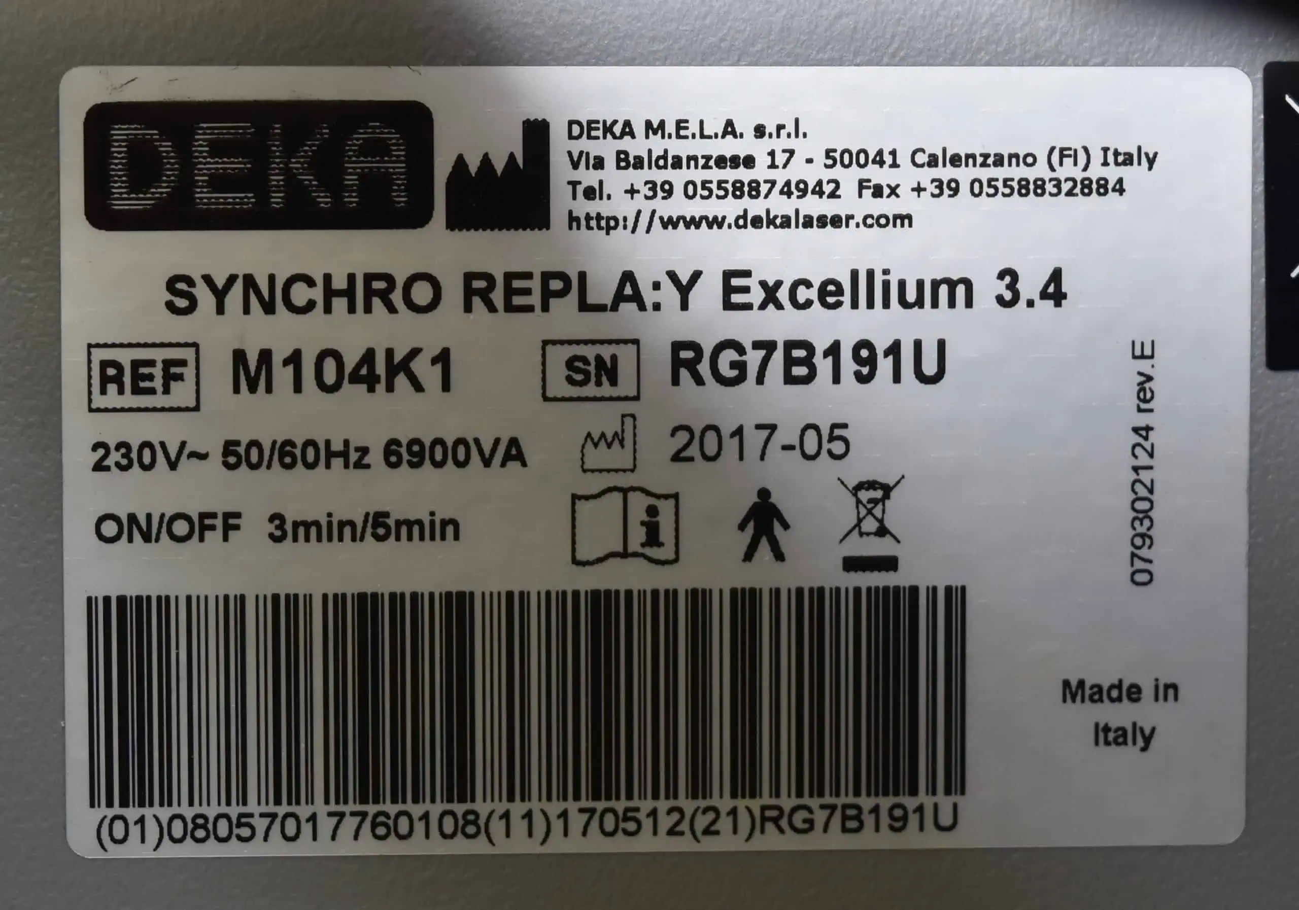 A close-up of a DEKA Synchro Replay device label displaying the model information, voltage, serial number, manufacturing date (2017-05), company address, contact details, and various warning and usage symbols.