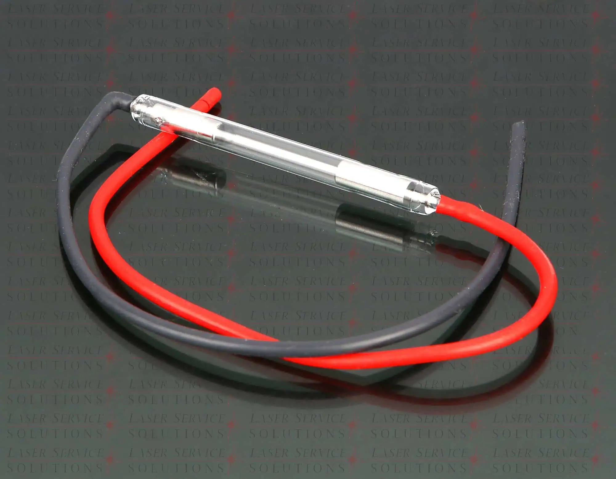 A Harmony Flashlamps cylindrical glass tube with metal ends is connected to one black and one red wire, all resting on a reflective surface. Faint repeating text appears in the background.