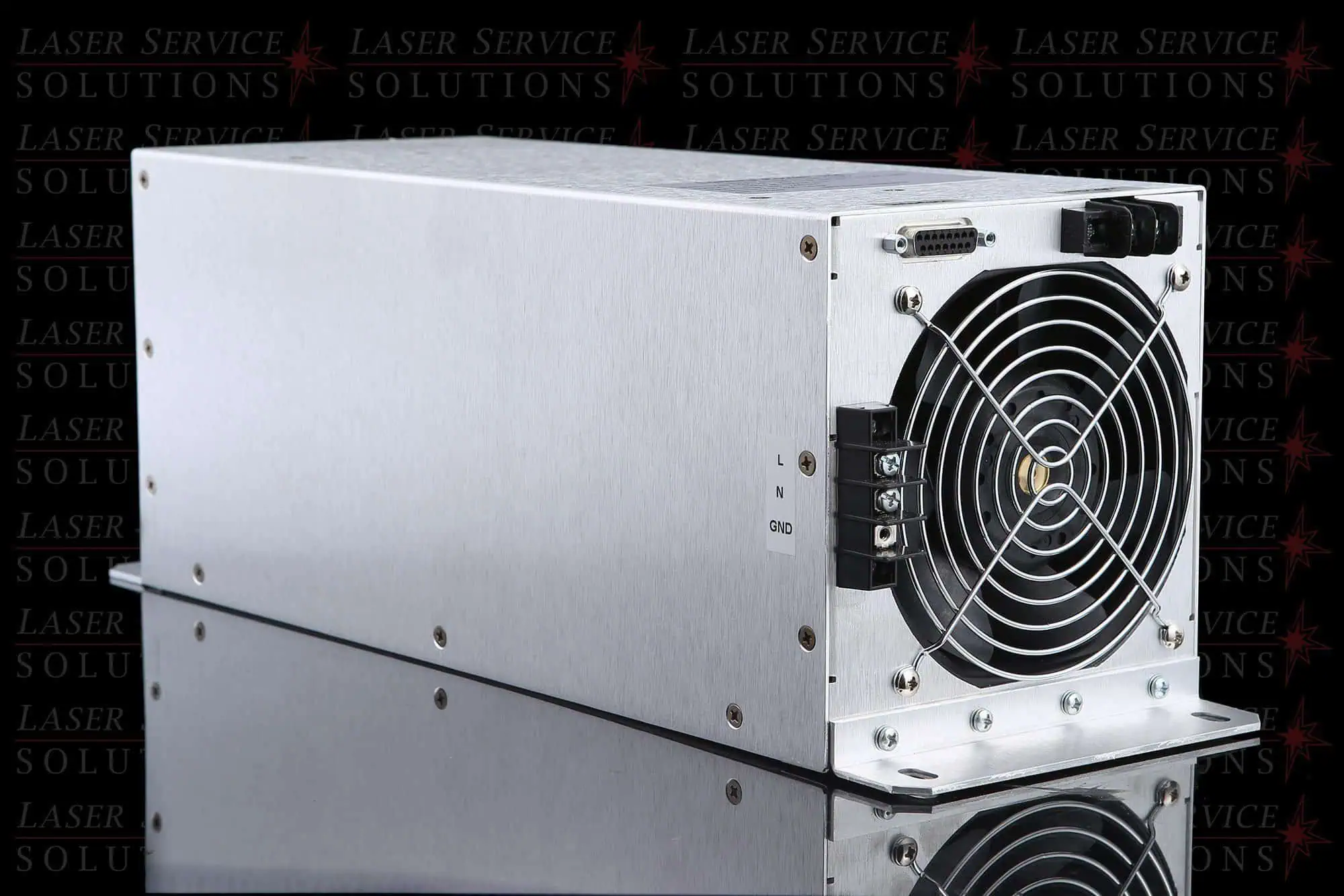 A Candela Mini GentleLase (MGL) HVPS, a rectangular metal electronic device featuring a large cooling fan, control ports, and screws on one end, is placed on a reflective surface against a background labeled Laser Service Solutions.