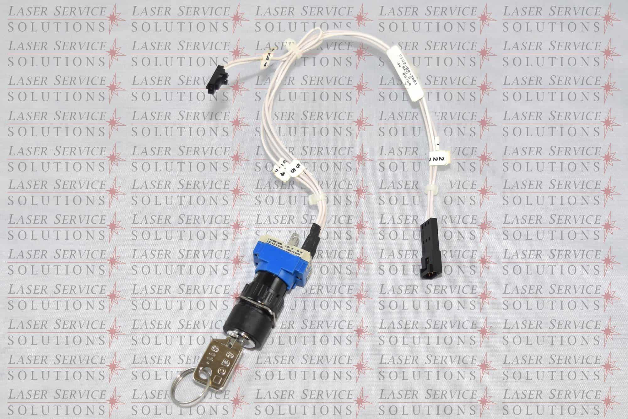 The Candela MGY Keyswitch Assembly is a wired electronic component featuring a blue plastic ring, metal connectors, and labeled white cables, shown against a background displaying repeated Laser Service Solutions text.