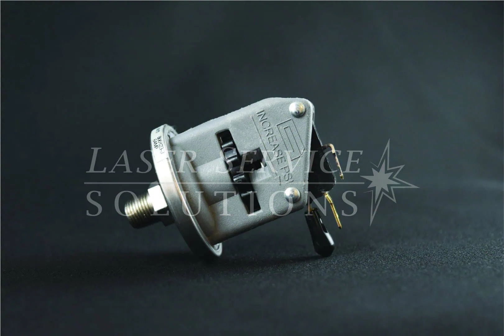A Candela Pressure Switch in gray, featuring a visible adjustment knob and electrical terminals, labeled with INCREASE and indicator marks, set against a black background.