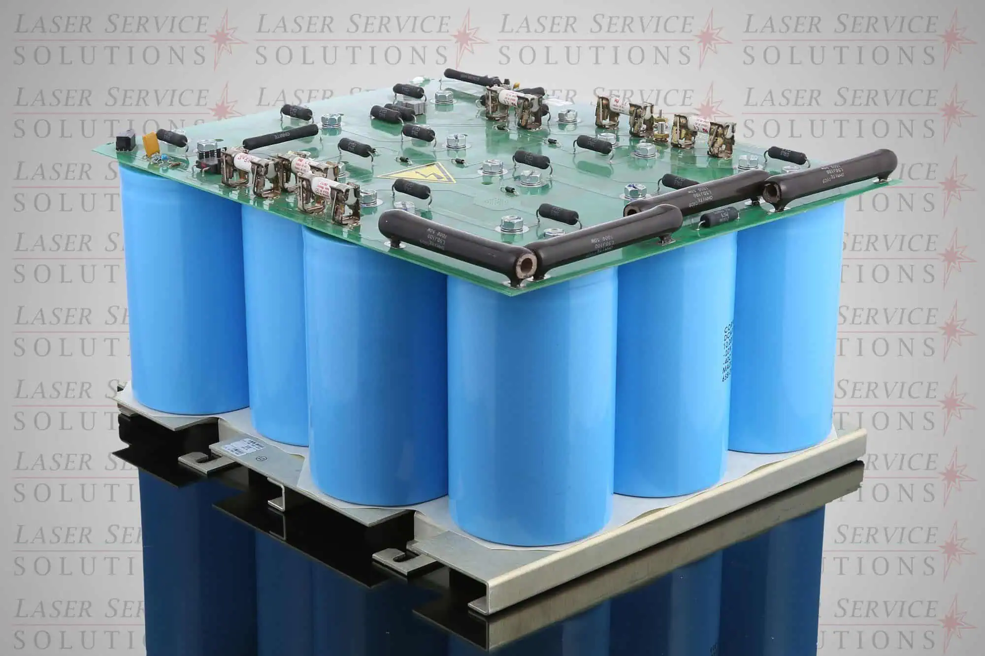 A Cynosure Elite+ Capacitor Bank Assy., a large electronic circuit board featuring multiple blue cylindrical capacitors and components mounted on a metallic base, is displayed with “Laser Service Solutions” watermarked repeatedly in the background.