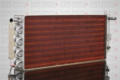 The Elite Heat Exchanger, featuring a rectangular metal design with copper coil fins and multiple pipe connections, stands on a reflective surface with “Laser Service Solutions” faintly visible in the background.