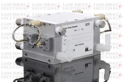 The Elite Pump Chamber is a rectangular metal laser pump chamber unit with tubes and connectors, displayed on a reflective surface against a background patterned with repeated Laser Service Solutions text. A white label featuring information fields is visible on one side.