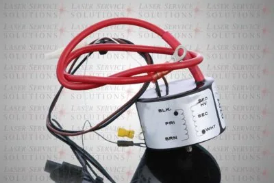 An Elite Trigger Transformer, a metallic electronic component featuring attached red, black, brown, and white wires, is displayed on a reflective surface with “LASER SERVICE SOLUTIONS” repeatedly printed in the background.